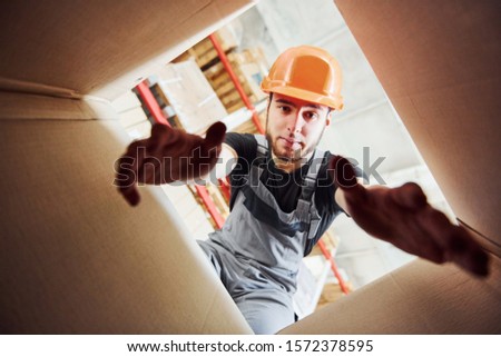 View from inside of paper box. Storage worker in hard hat looks down.