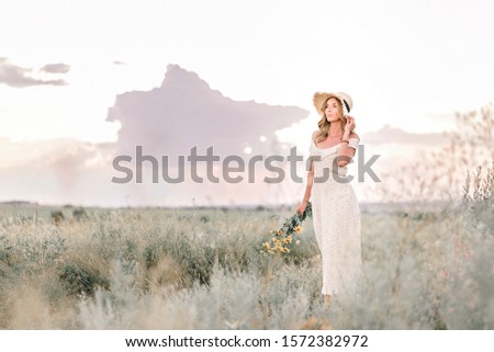 Cute blonde woman in straw hat with flower bouquet in the summer field. Being outdoors.
