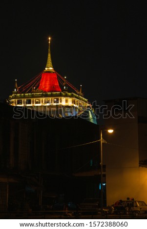 Vertical picture of The Golden Mount Temple with red cloth at Wat Sa Ket at night over low buildings around temple, one of the most travel Landmark of Bangkok Thailand.