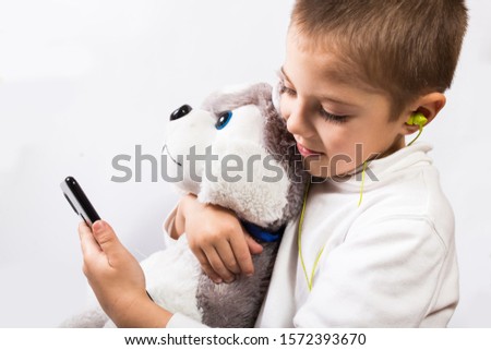 Phone addicted little boy with plush toy and with earphones on white background