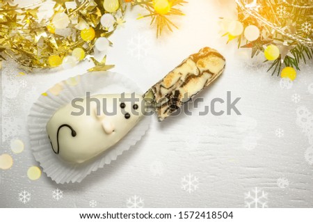 Cake in the form of a white mouse who eats Turkish delight with marzipan, lying on the green branches of a Christmas tree with lights bokeh. Symbol of 2020. Copy space