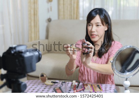 Young woman using makeup brush to apply highlighter while recording video for everyday makeup tutorial. Focusing on makeup brush.