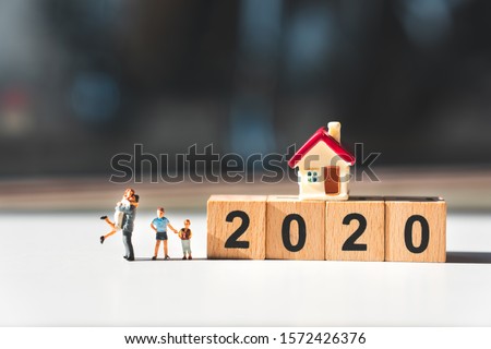 Miniature people, happy family standing with mini house on wooden block 2020 using as family and property concept