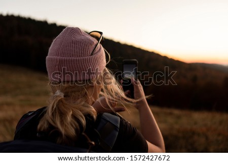 Portrait of beautiful young woman whos relax in mountains. girl takes pictures by cell phone. A beautiful sunset in the bosom of nature.