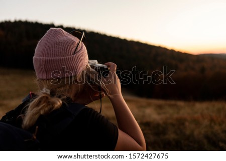 Portrait of beautiful young woman whos relax in mountains. girl takes pictures by camera. A beautiful sunset in the bosom of nature.