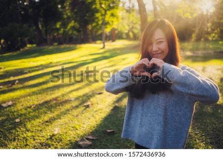 A beautiful asian woman making heart hand sign in the park before sunset