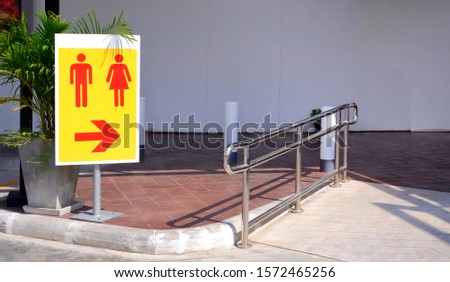 Restroom sign on metal pole with stainless steel fence on the different level ground in public area