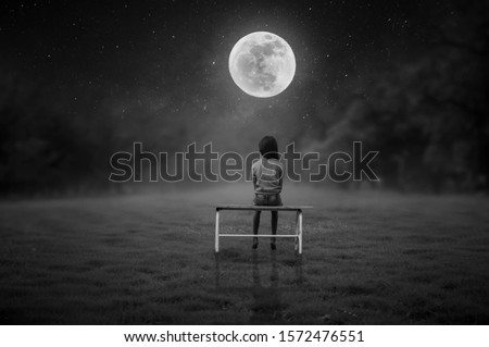 A black and white picture of a little girl sitting in a chair in the middle of the lawn.