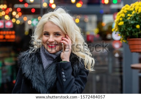 Young beautiful blonde woman talking on smartphone against festive lights background. The concept of Christmas time. Copy space - image