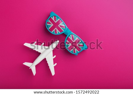 Turquoise sunglasses with United Kingdom flag in lenses on crazy pink background with white airplane. T