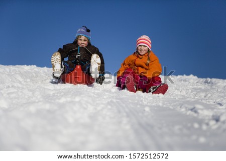 Boy and girl tobogganing in snow
