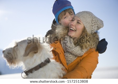 Mother laughing with son and pet dog in snow