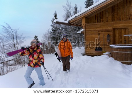 Couple walking with skis outside log cabin