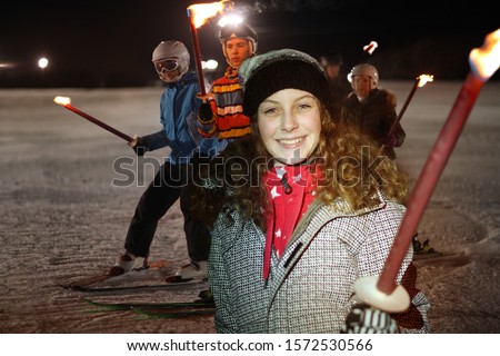 Girl holding flaming torch on ski slope at night, portrait