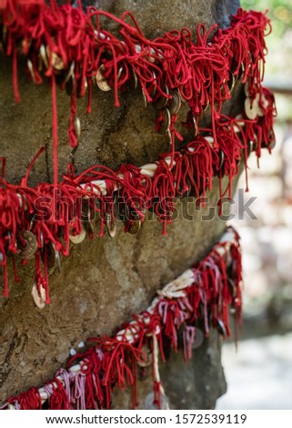 Five-yen coins hang off scarlet string draped over a boulder at Kuzuharaoka Shrine, Kamakura, Japan