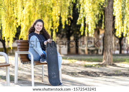 Cute teen sitting on a bench with her skate board