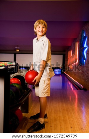 Boy in a bowling alley holding a red bowling ball