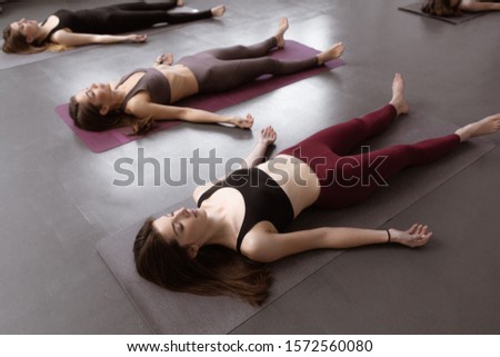 Fitness female group doing practicing in a yoga class. Shavasana or corps pose, yoga practice. Royalty-Free Stock Photo #1572560080