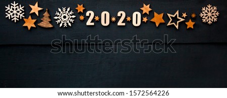 The beautiful christmas background with a lot of small wooden decorations and wooden numbers 2020 on the dark wooden desk.
