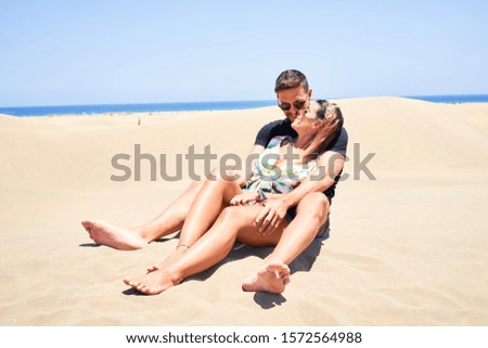 Young beautiful couple smiling happy and confident. Sitting with smile on face hugging at the beach