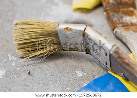 A brush with rusty metal lying on the concrete floor with blue and yellow fabric underneath