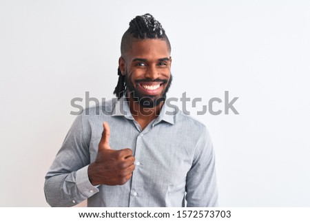 African american businessman with braids standing over isolated white background doing happy thumbs up gesture with hand. Approving expression looking at the camera with showing success.