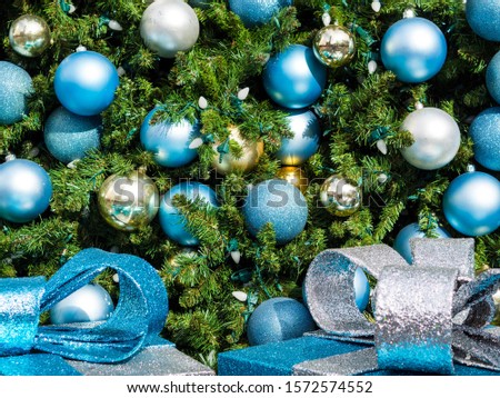 Close-up of Christmas tree, adorned with blue, silver and gold balls and topped with a star on the cusp of the tree. At the foot of the tree there are blue and silver glitter gifts.