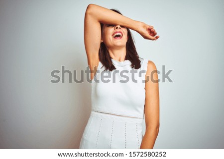 Young beautiful woman wearing dress standing over white isolated background covering eyes with arm smiling cheerful and funny. Blind concept.