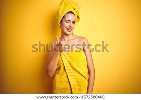 Beautiful woman wearing shower towel on body and head over yellow isolated background doing happy thumbs up gesture with hand. Approving expression looking at the camera showing success.