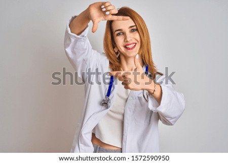 Redhead caucasian doctor woman wearing stethoscope over isolated background smiling making frame with hands and fingers with happy face. Creativity and photography concept.