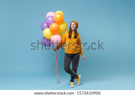 Cheerful young woman girl in sweater hat posing isolated on blue background studio portrait. Birthday holiday party people emotions concept. Mock up copy space. Celebrating hold colorful air balloons