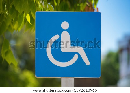 Disability parking, street post sign for reserved parking sign outside on a sunny day with green foliage and blue sky
