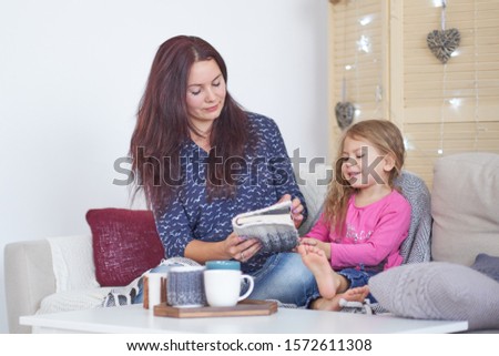 Mom and daughter are sitting on the sofa at home and reading a book. Happy loving family. Mother and her daughter child girl playing. Good time at home.