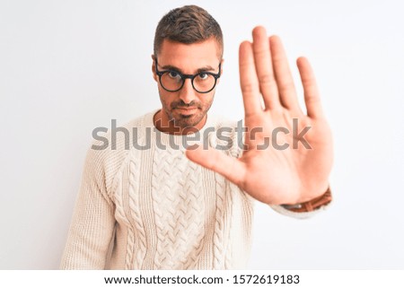 Young handsome man wearing glasses and winter sweater over isolated background with open hand doing stop sign with serious and confident expression, defense gesture