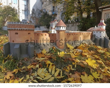 Model of an ancient fortress on the background of modern houses. Yellow autumn leaves in the meadow. Sun glare on the grass. Park in late autumn.
 
Fall season beauty.