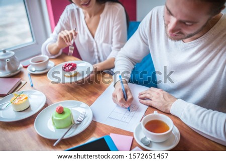 Businessman making notes. Businessman making notes while revising desserts for their menu with wife