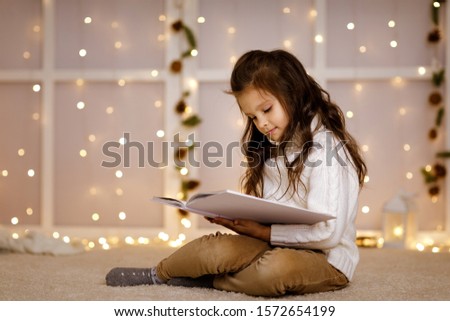 Happy little child girl is reading fairy tale book on the background with lights. Merry Christmas. space for text