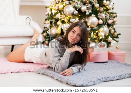 Cute girl in   light sweater near   Christmas tree.