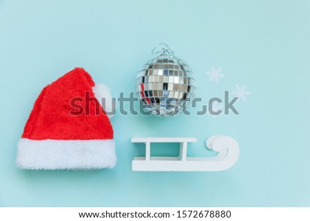 Simply minimal composition winter objects ornament Santa hat sled ball isolated on blue pastel trendy background. Christmas New Year december time for celebration concept. Flat lay top view