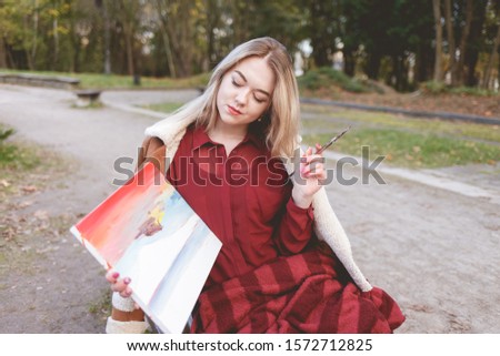 Young girl draws a picture on a park bench. Blonde artist engaged in her favorite hobby of drawing