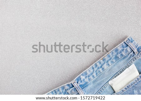 white women's pad in the package in the back pocket of jeans on a silver gray background