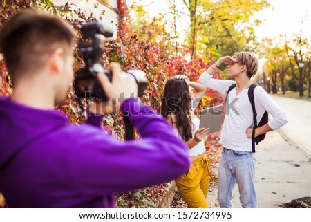 Man photographing his friends or young couple with professional camera while using digital tablet on the street