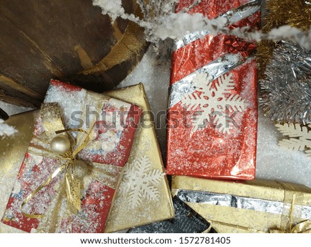 Christmas decoration with several gift boxes sprinkled with glitter decorated with snowflakes decorations next to a tree trunk which is left in the picture above.