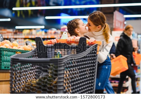 beautiful mother holding grocery basket with her child walking in supermarket. Shopping for healthy.