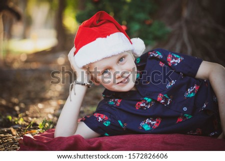 Child dressed in Christmas outfit  on  red blanket in the park with a decorated Christmas tree in the background