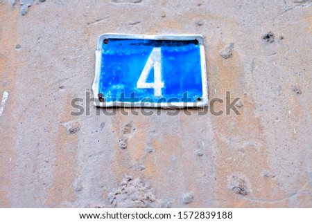 Number 4, four, blue plate on a pale weathered wall.