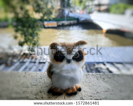 The image of a furry owl toy doll stands on the edge of the back porch in the morning, taken with blurred background.