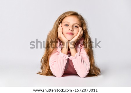 Portrait of a young teenage girl in a long-sleeved pink dress and matching tone gumshoes lying on the floor, isolated on a white background. She folded her head in her hands and looks into the frame