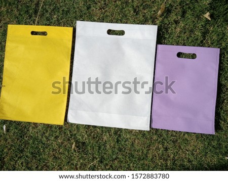 3 different color Non Woven Eco Friendly Bags on Green Grass Background. Shopping & Gift Bags