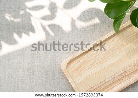 A blank wooden tray neatly arranging on linen table cloth, with the space show sunlight and beautiful leaves shadow. Background with copy space for natural and minimal products. Soft and calm concept
